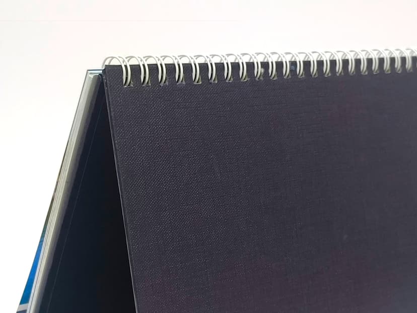 Close-up of the white wire-o binding and the dark textured rexine stand.